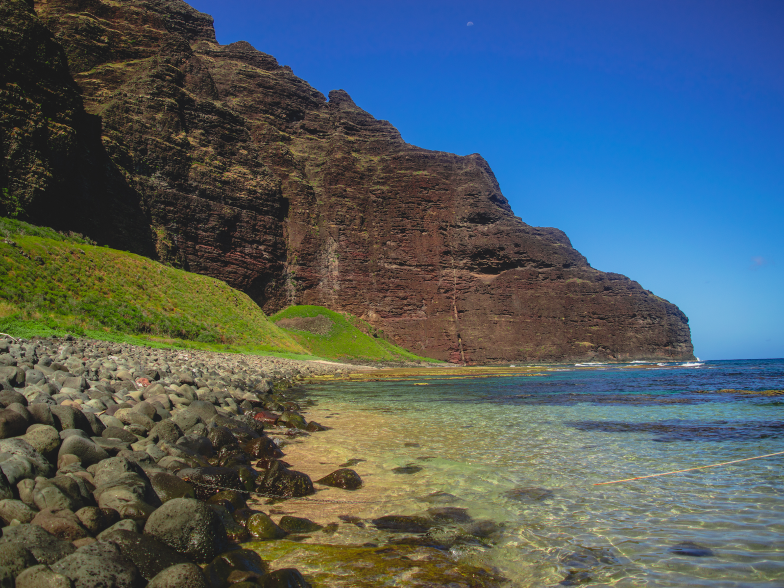 rocky shore of Nualolo Kai Beach, titled one of the best snorkeling spots in Kauai, near a tall cliff