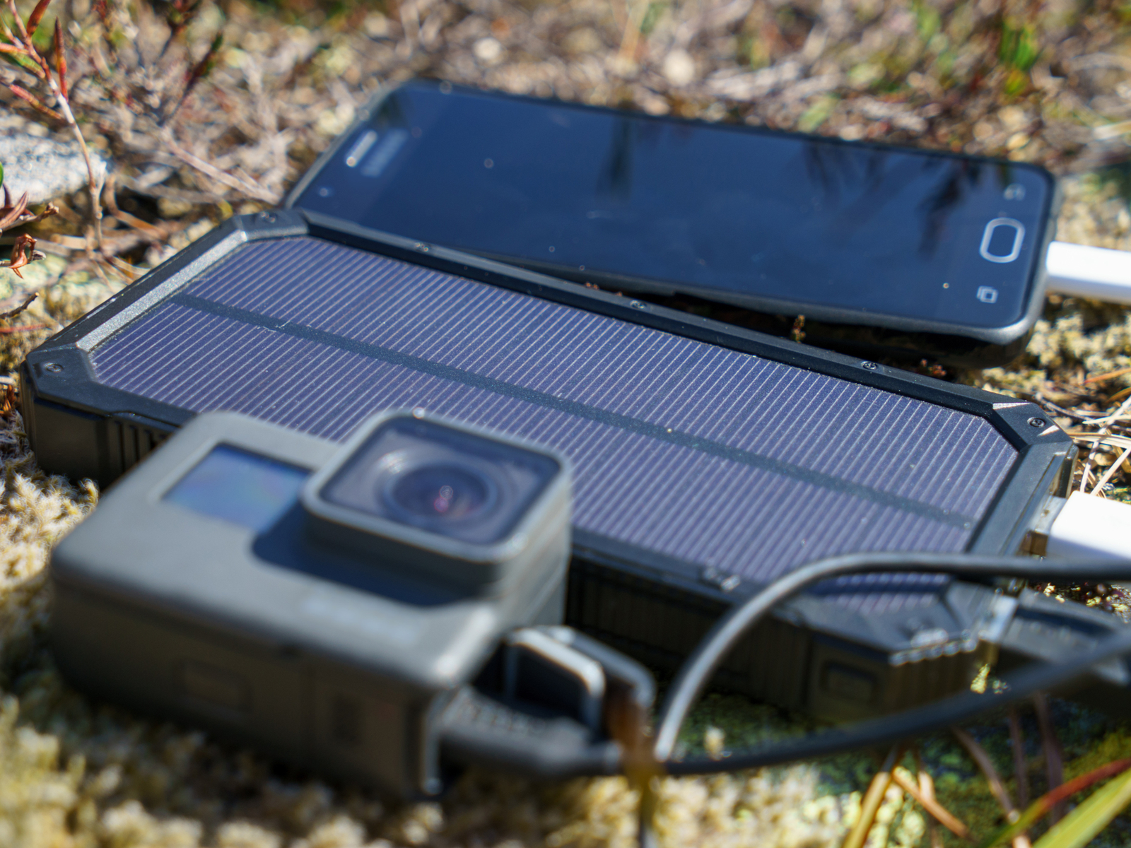 Photo of one of the best solar power banks charging an action cam and phone on some grass