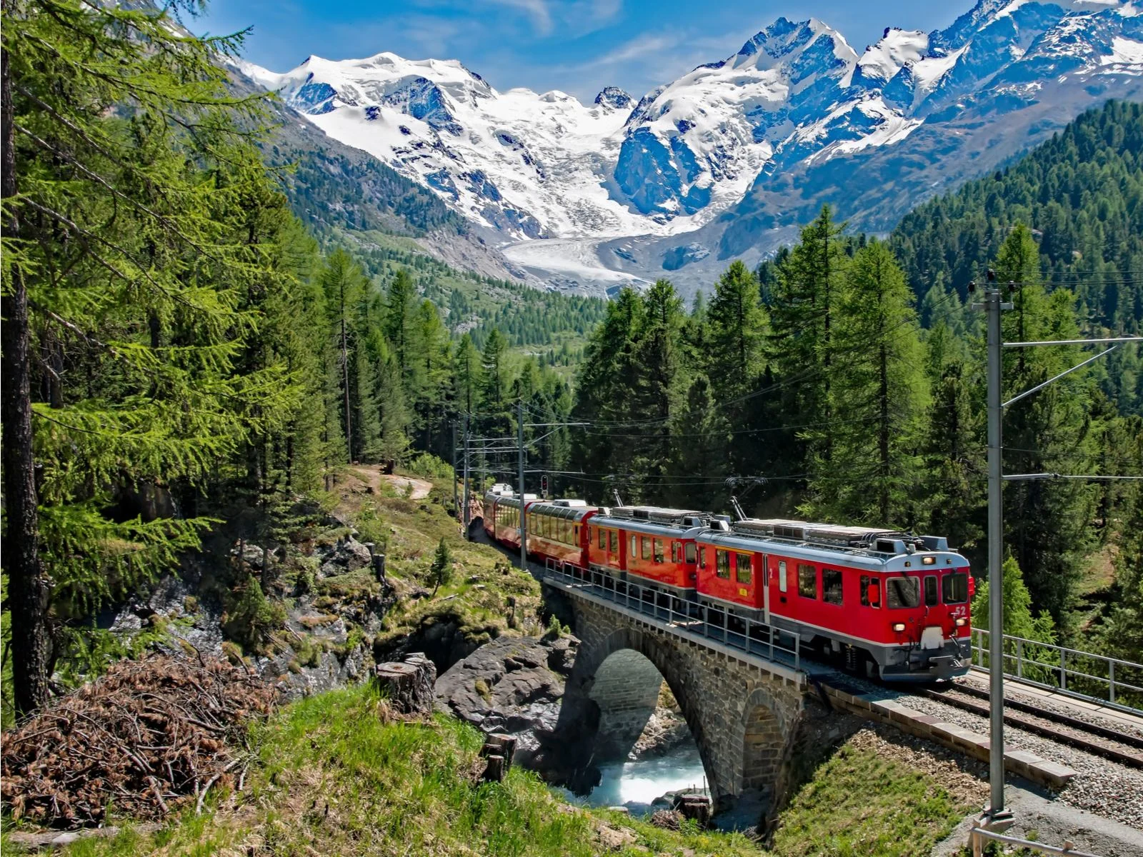 The Bernina Express pictured during the best time to visit Europe with the gorgeous Alps in the background of the forest