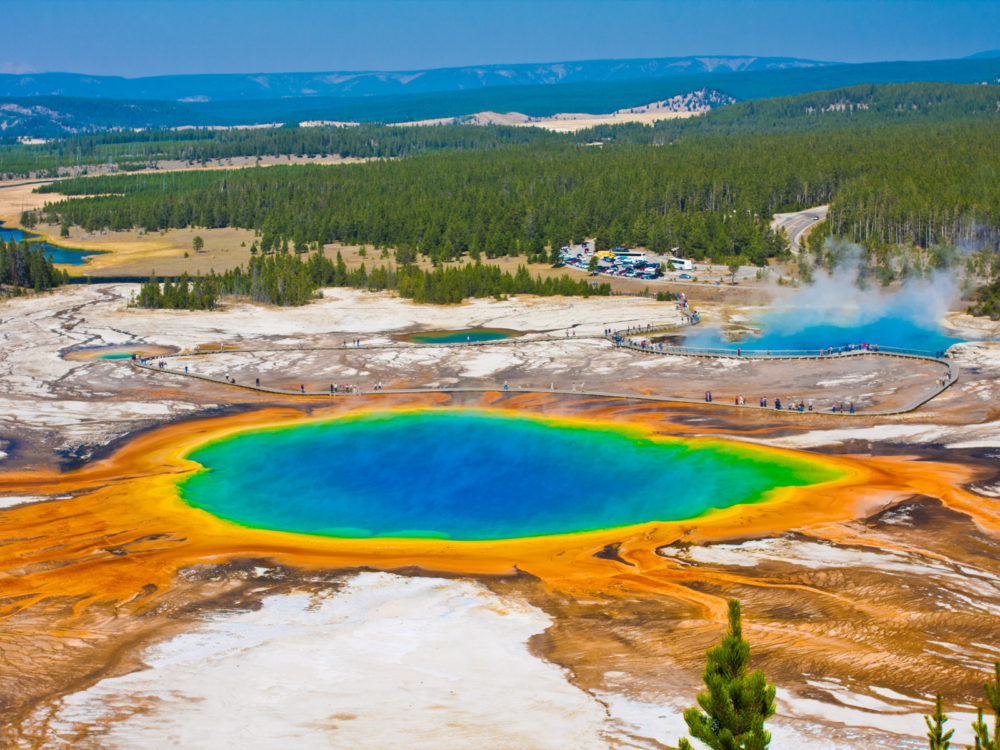 Tourists walking on a looped path beside the steamy vibrant Grand Prismatic Spring in Yellowstone National Park, one of the most iconic places in America