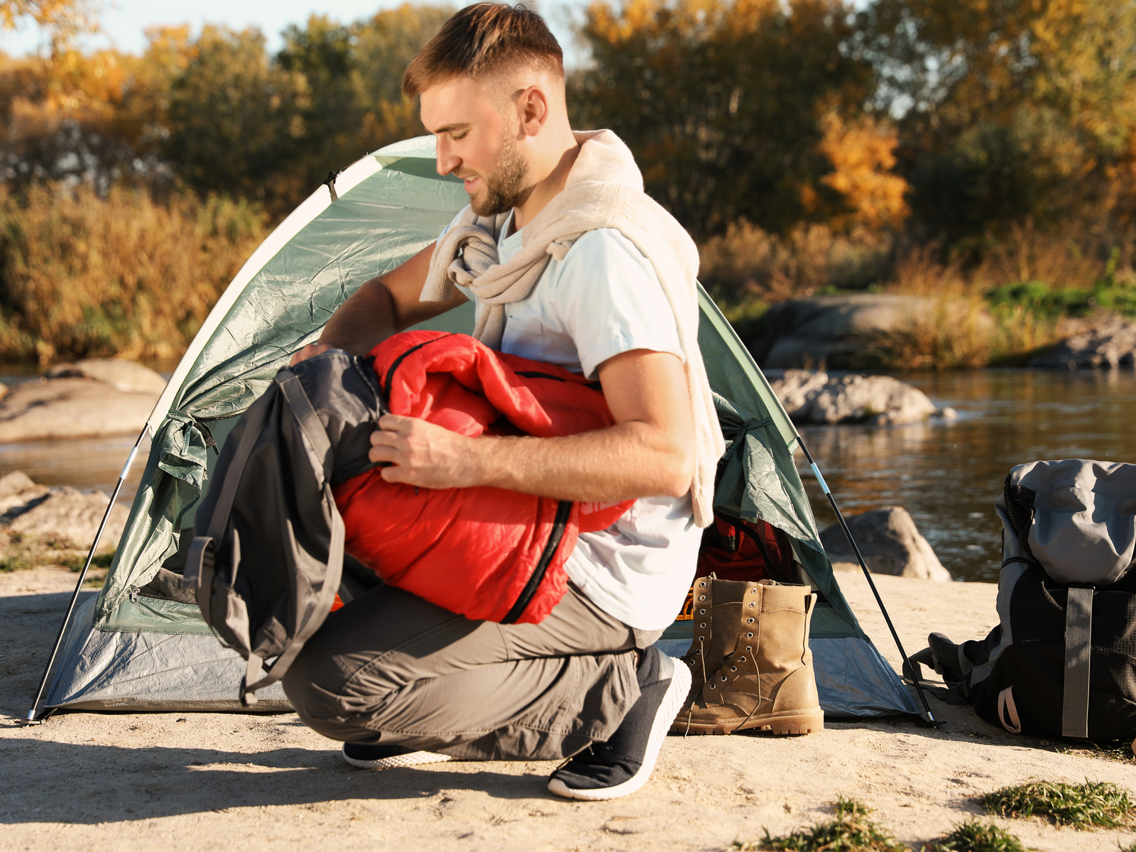 Young man packing his sleeping bag near his camping tent