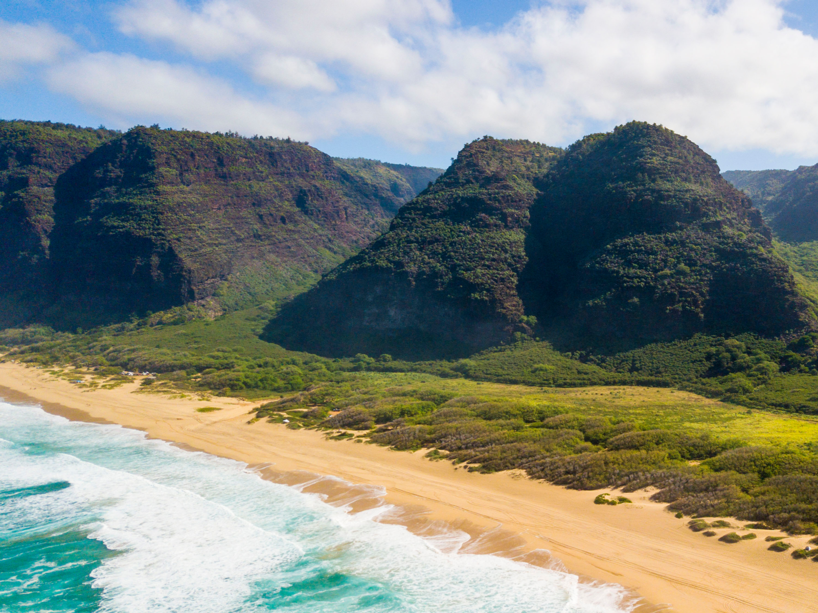 Iconic tree-covered hills and the foamy golden sand shore of Polihale Beach south of NaPali coast, considered one of the best beaches in Kauai