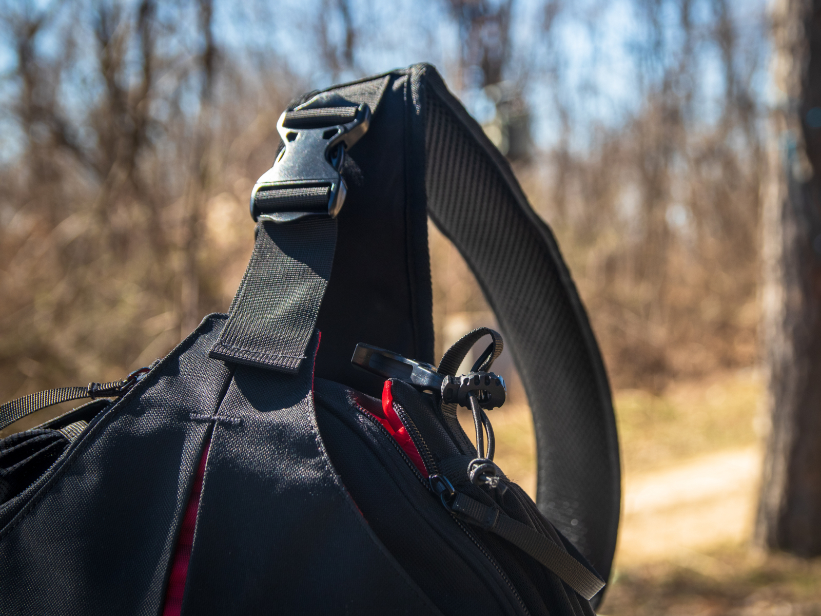 Sling bag (also called one of the best EDC bags) pictured on the ground in a park next to a tree with a blurry background