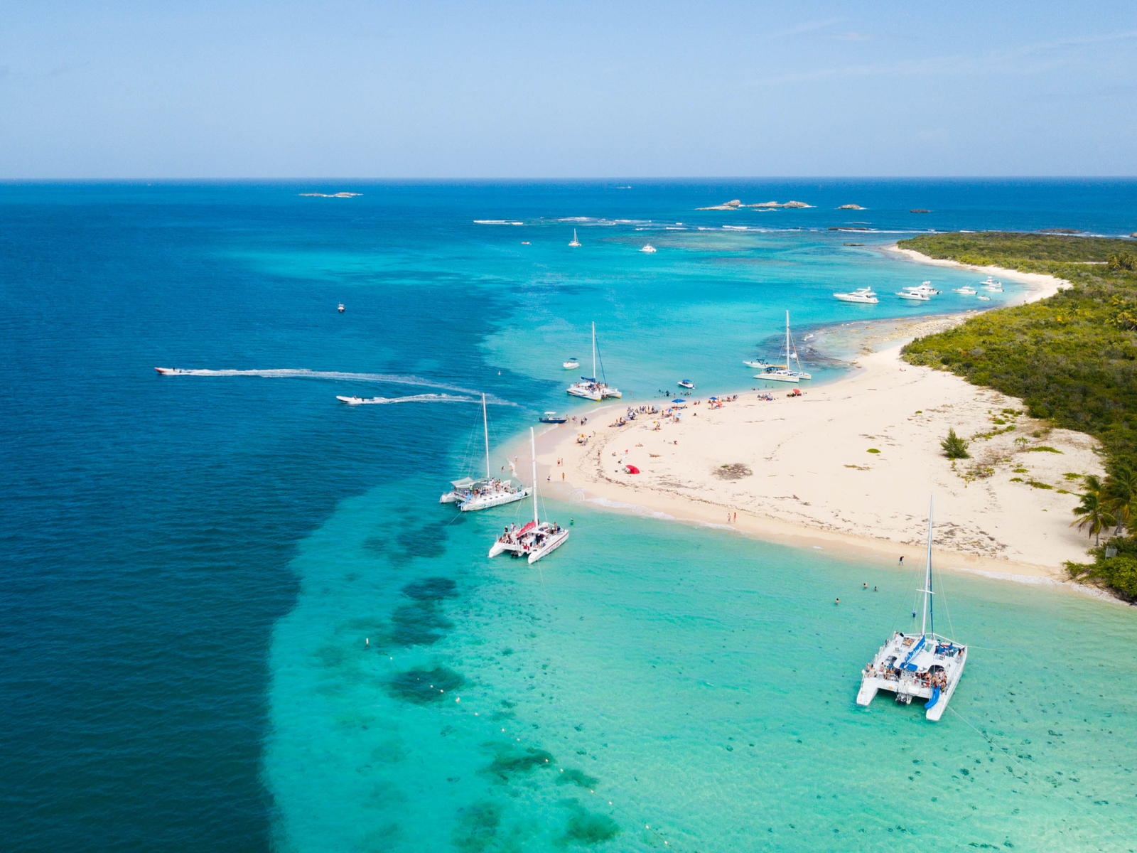 Passenger boats docked on the shallow clear water and two speedboats rushing at a distance from the isolated island of Cayo Icacos. considered one of the best places to visit in Puerto Rico