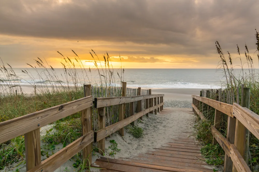 Sunrise lights up the sky over a wooden boardwalk with grasses and sand at Myrtle Beach for a section detailing weather and conditions month by month
