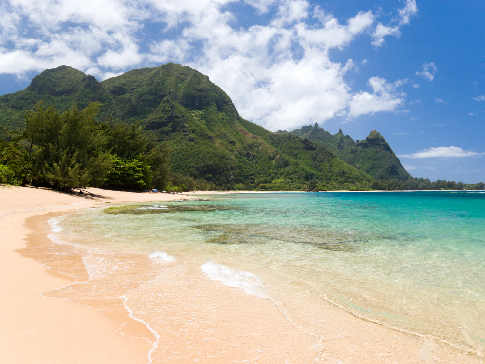 Fine sand at the secluded Haena Beach with a unique mountain formation covered with trees, one of the best beaches in Kauai
