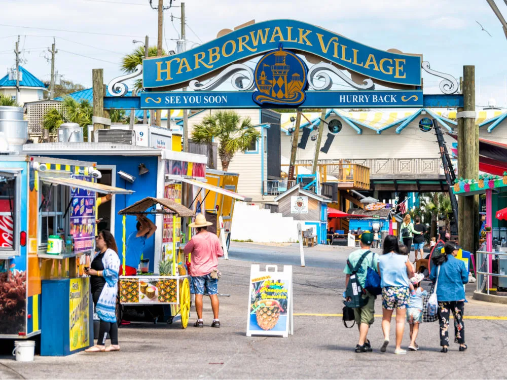 People walk under the Sign for Harborwalk Village in Emerald Grande during the best time to visit Destin Florida