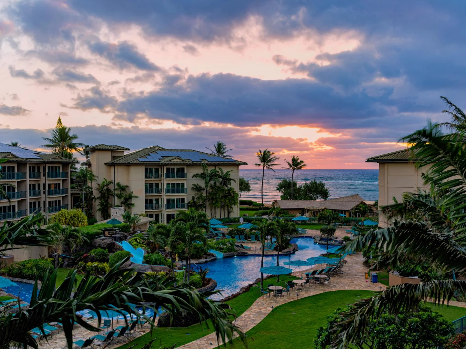 Young sunrise over the beachfront Waipouli Beach Resort, one of the best hotels in Kauai, in frame are its resort structures and blue irregularly shaped pool