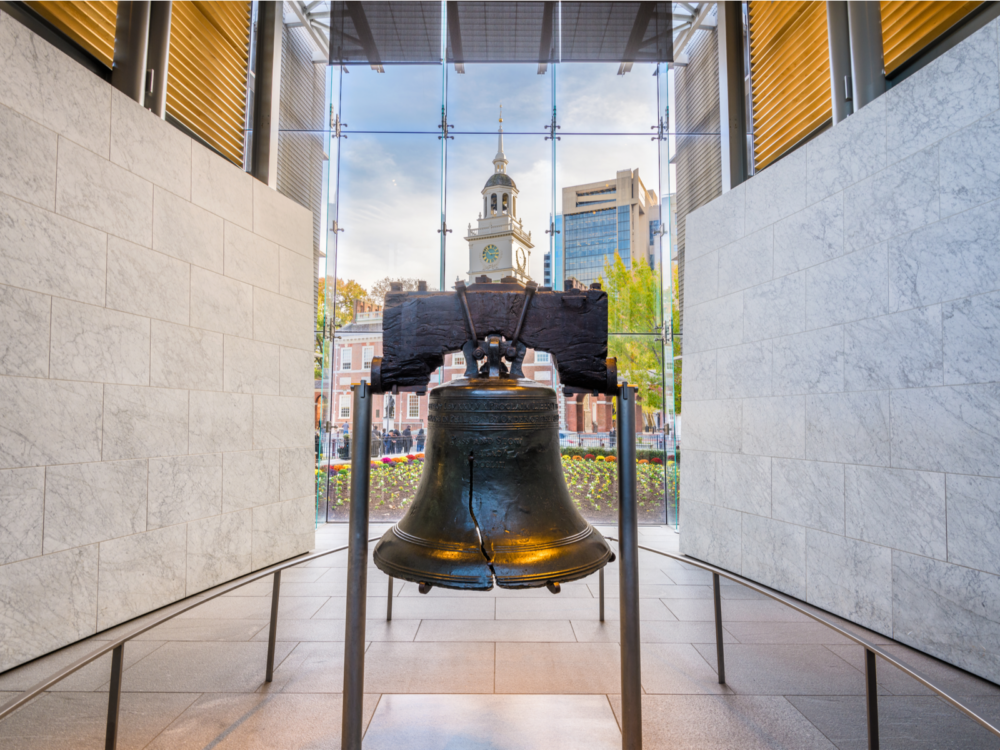 Historic Liberty Bell, making Philadelphia in Pennsylvania one of the most iconic places in America, exhibited in a tiled room where building exterior can be seen through glass panes