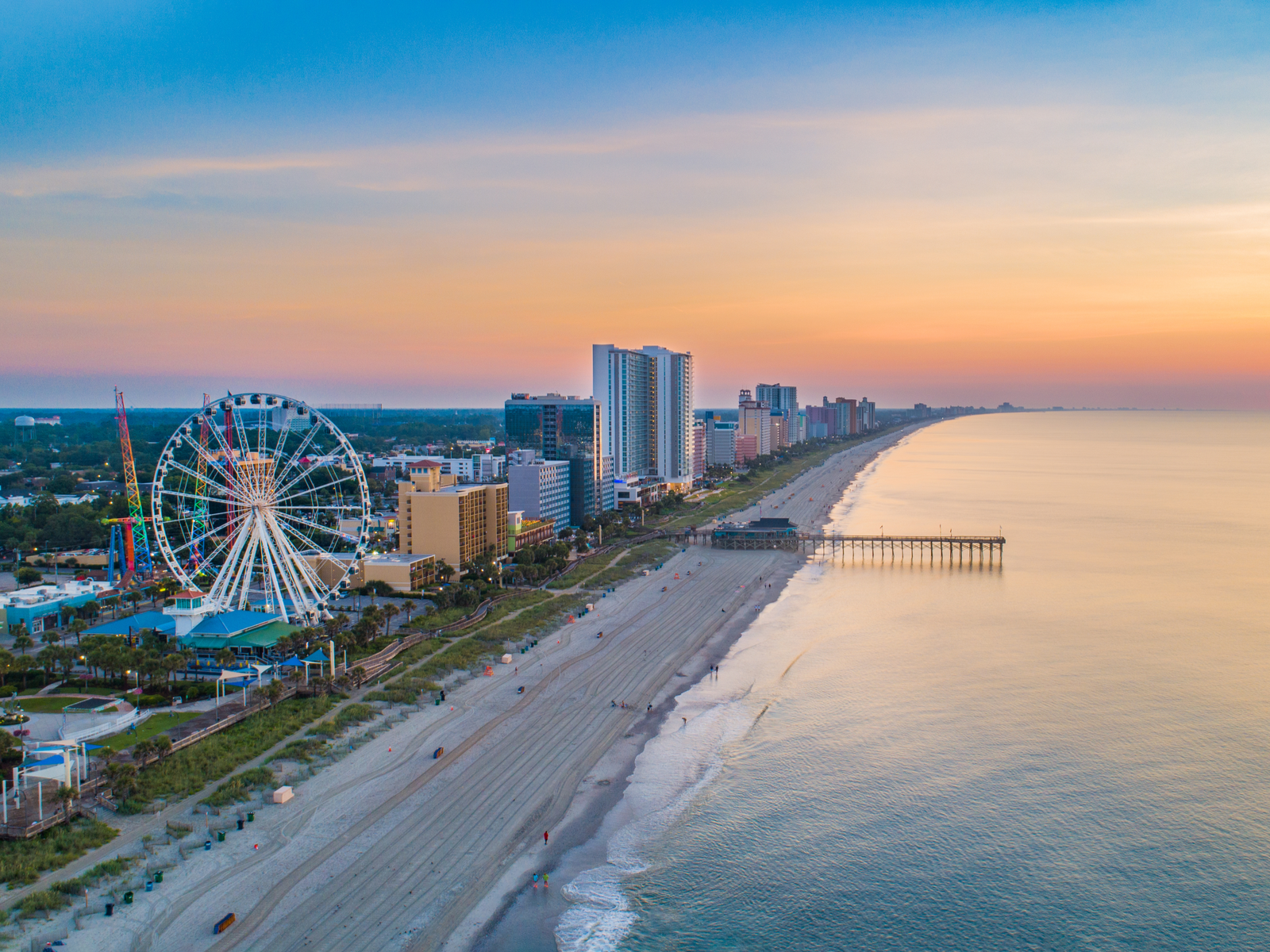 Sunset over the Myrtle Beach in South Carolina, a piece on the best beaches on the East Coast, seen with its dock, gigantic ferris wheel, and row of hotels at its coast