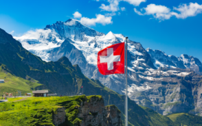 Waving Swiss flag in the foreground while tourists look at the peaks of Monch and Jungfrau from a viewing point