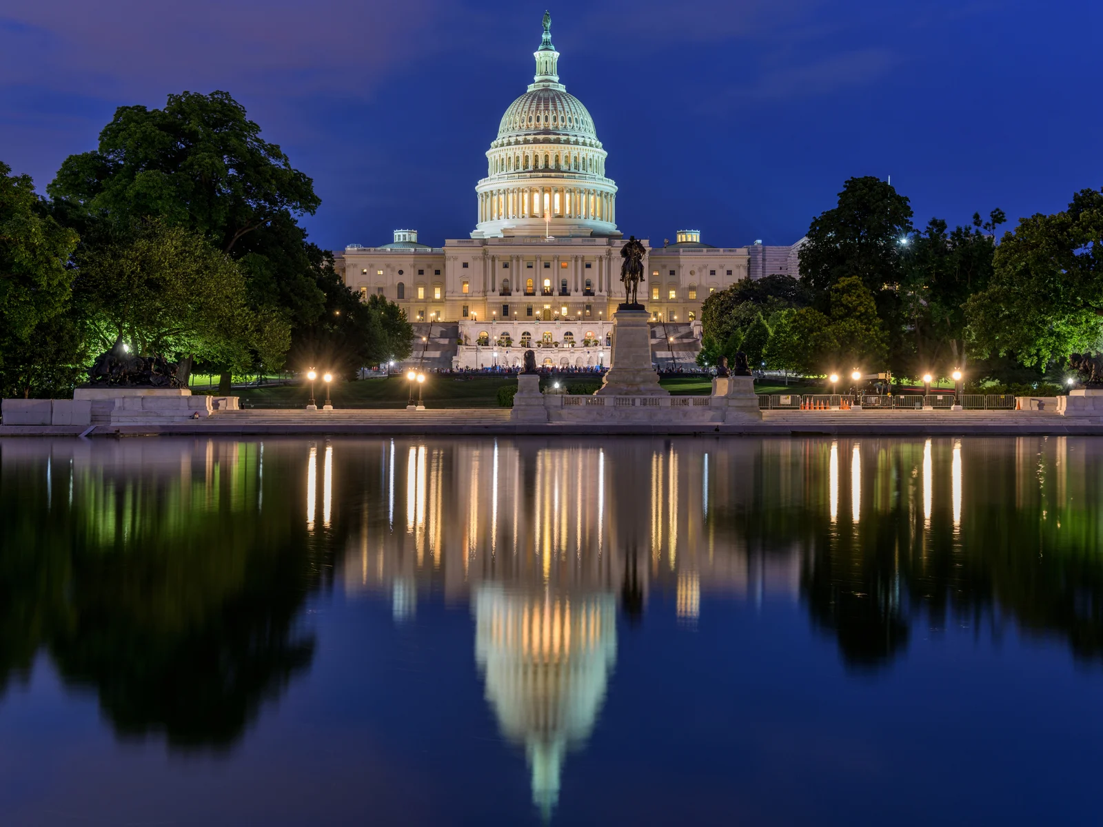 A crowd gathering during dusk at one of the best things to do in Washington, D.C., the U.S. Capitol Building which is reflected on the reflection pool