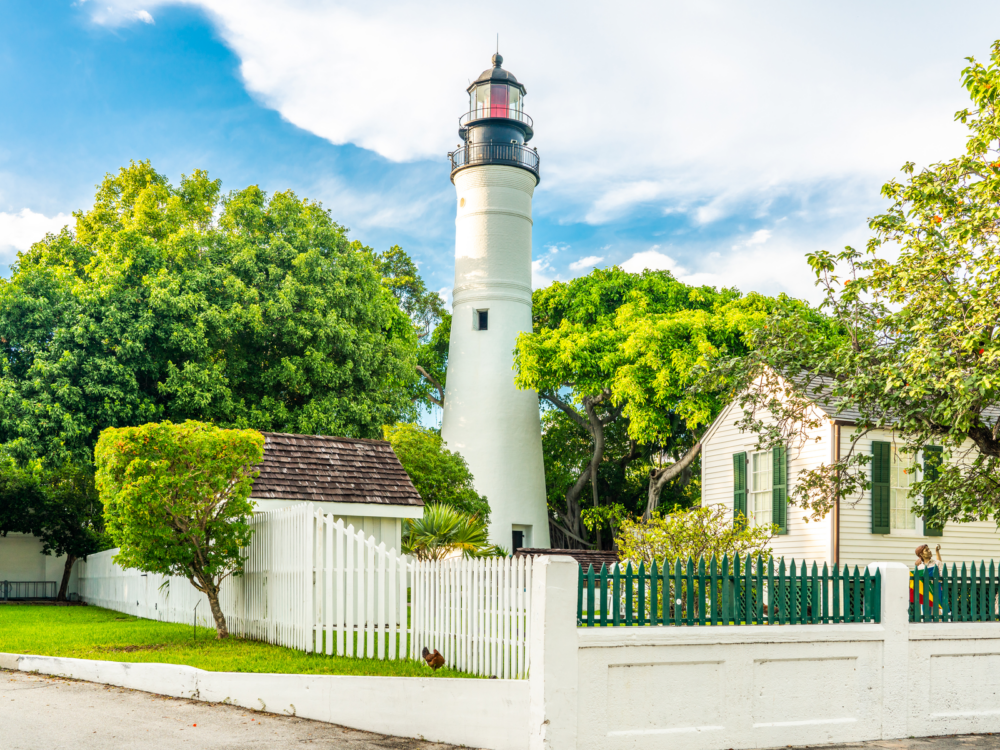 White lighthouse and residential house inside a fenced lot, Key West Lighthouse Museum as one of the best things to do in Key West