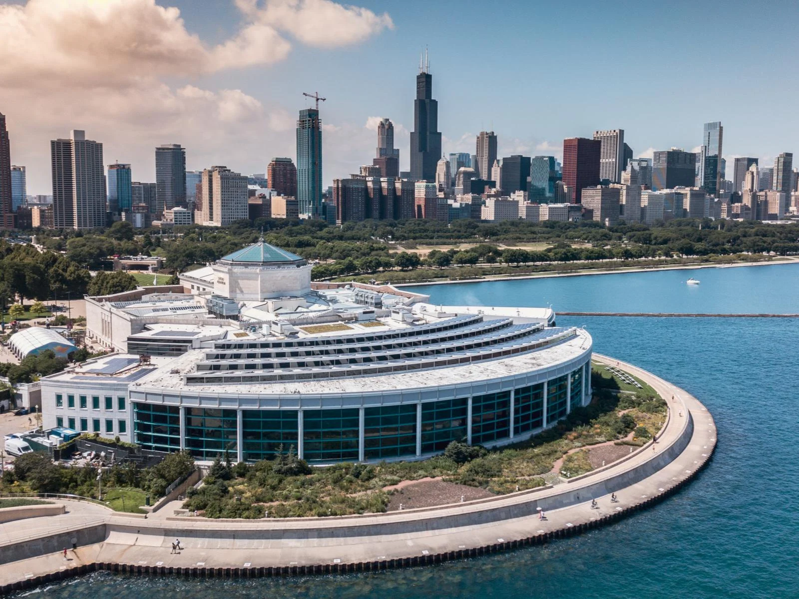 Aerial view of the rounded architecture on Shedd Aquarium, one of the best aquariums in the US, with the Chicago skyline in the background and a few people walking along the seaside pathway
