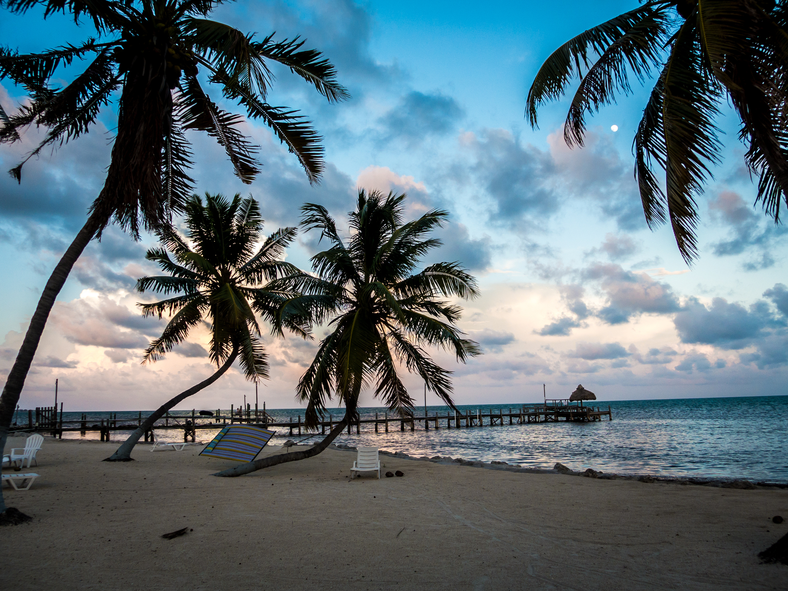 Shot on a cloudy and lackluster day of a beach with palm trees and a dock jutting into the water during the worst time to visit the Florida Keys