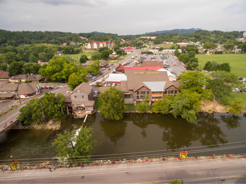 Aerial image of the Old Mill Square, one of the best things to do in Pigeon Forge, on a cloudy day as seen from above the river