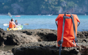 Orange waterproof day bag sitting on the rocks in front of kayakers on the ocean