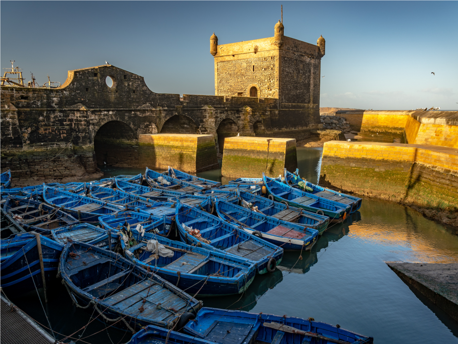 Sunset over the older Essaouira Citadel, a Game of Thrones filming locations you can visit, where used blue fishing boats and docked