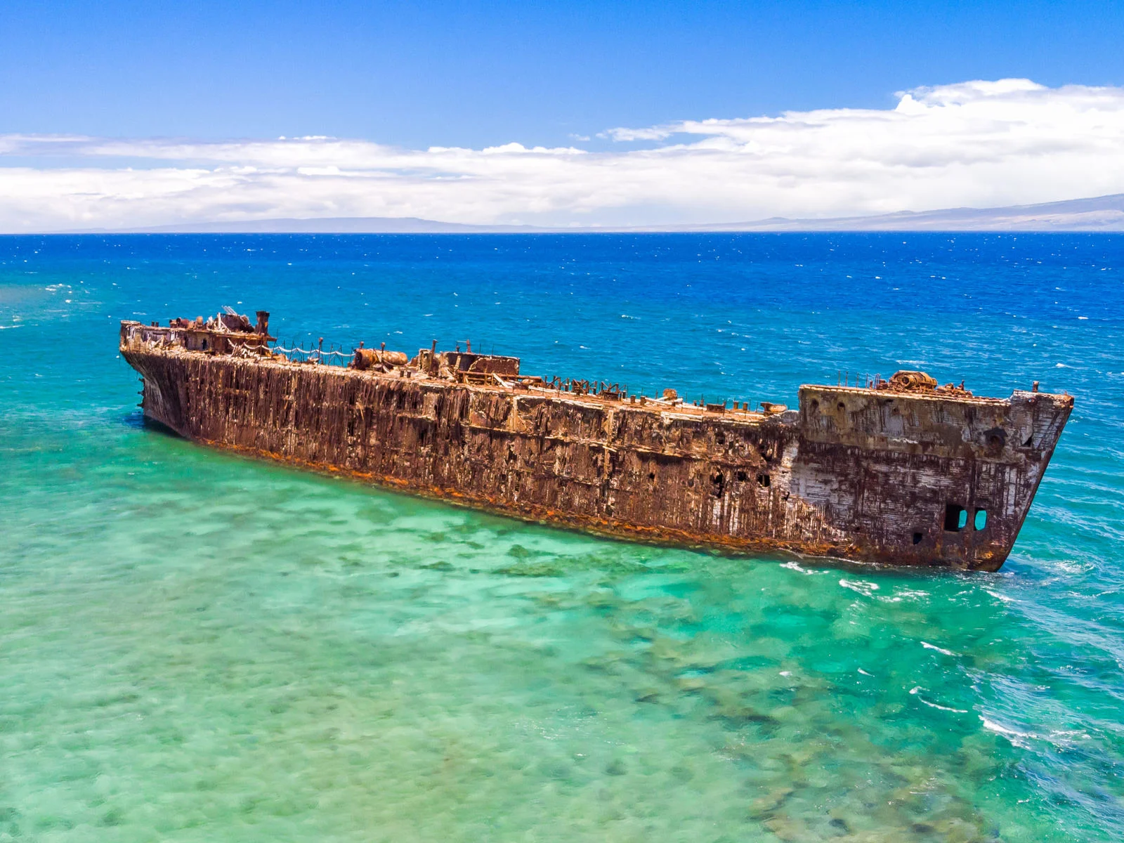 A corroding rusty old abandoned ship off the coast of crystal clear Shipwreck Beach, one of the best beaches in Kauai