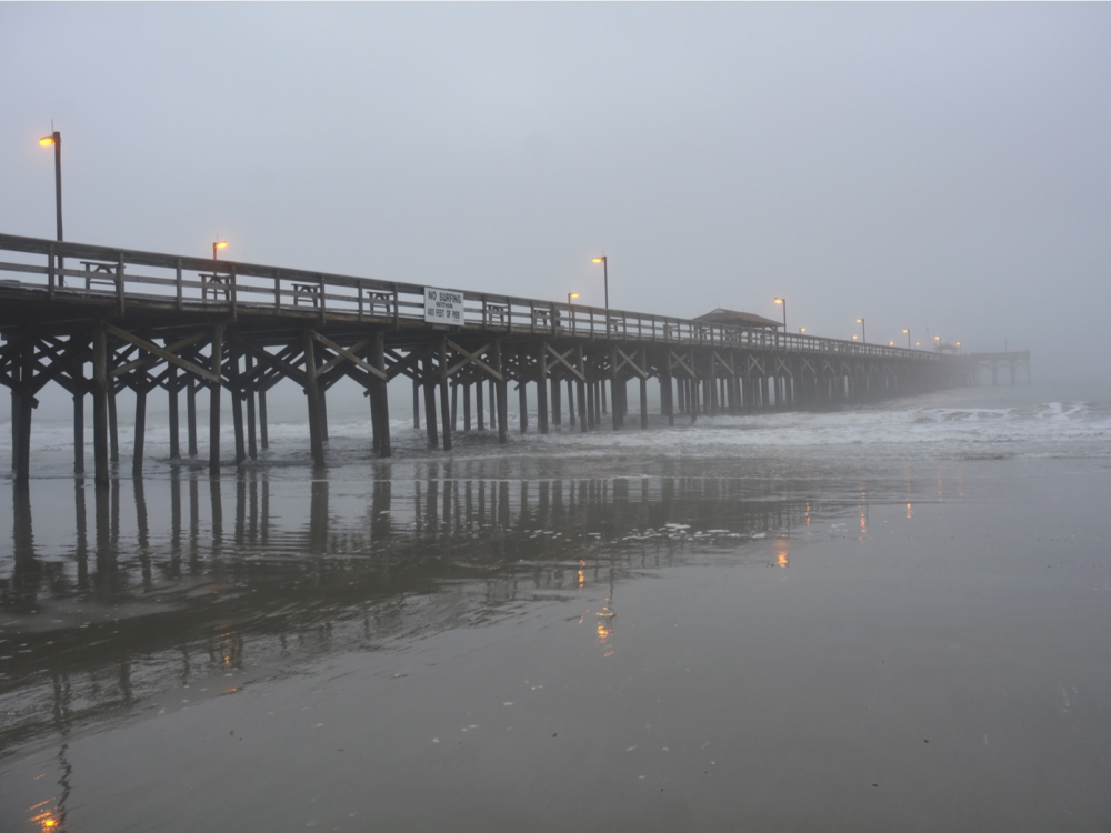Fishing pier jutting into the ocean on a stormy day during the worst time to visit Myrtle Beach