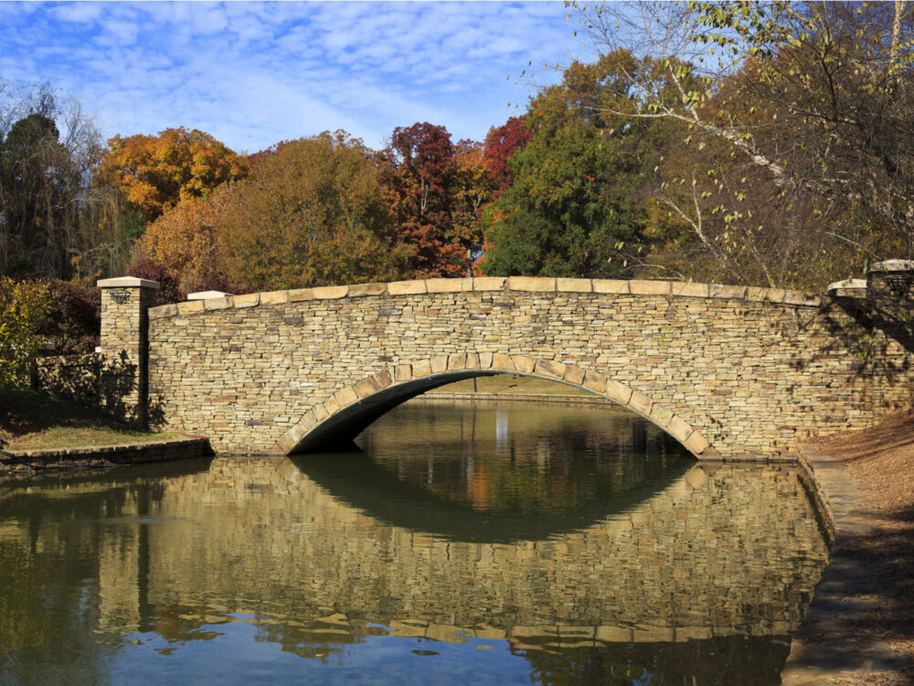 a short solid stone bridge crossing a calm lake in freedom park, one of the best things to do in charlotte, nc, with trees in background