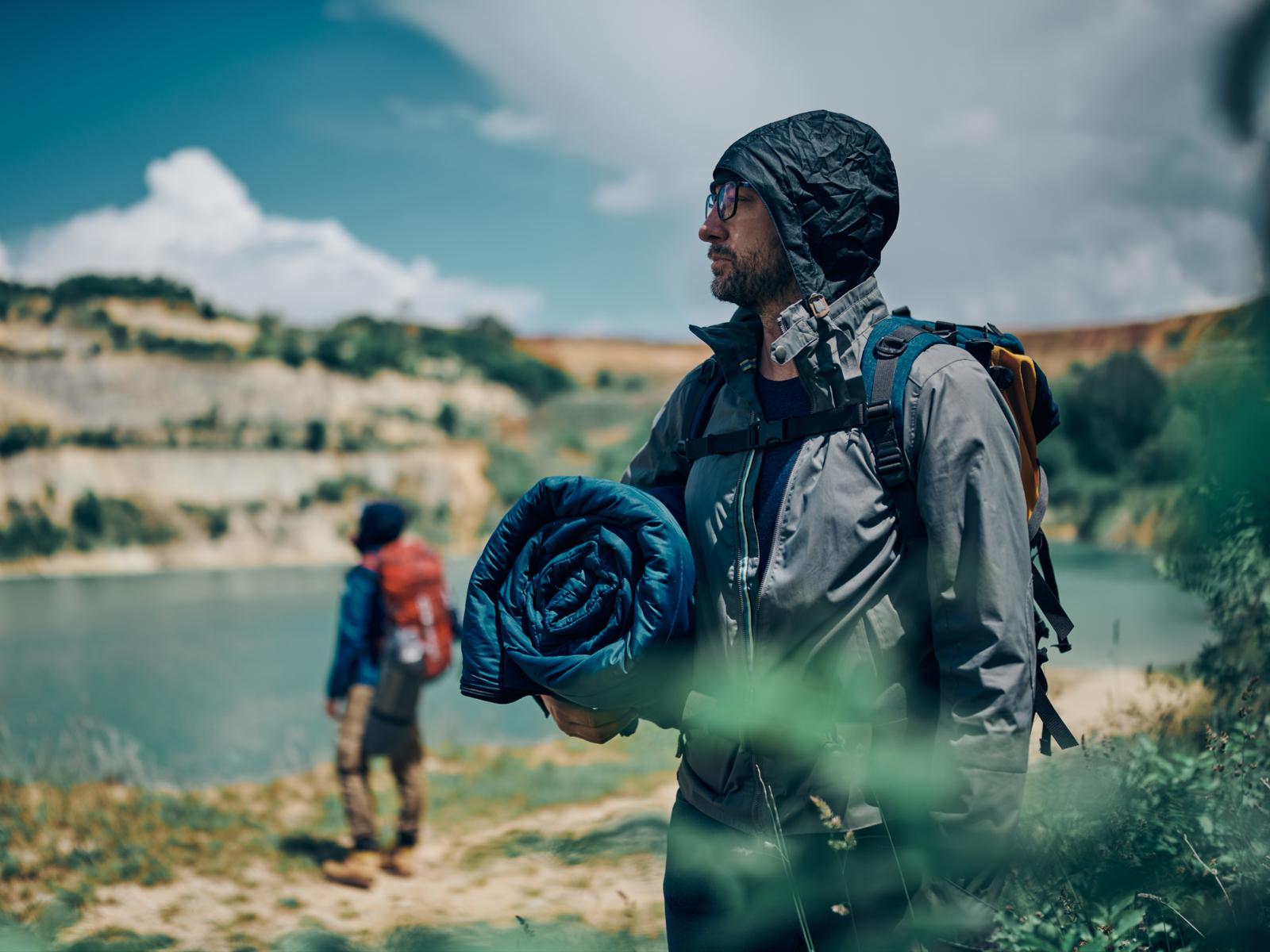 Young handsome man standing in nature holding his backpack sleeping bag on a clear and slightly cloudy day