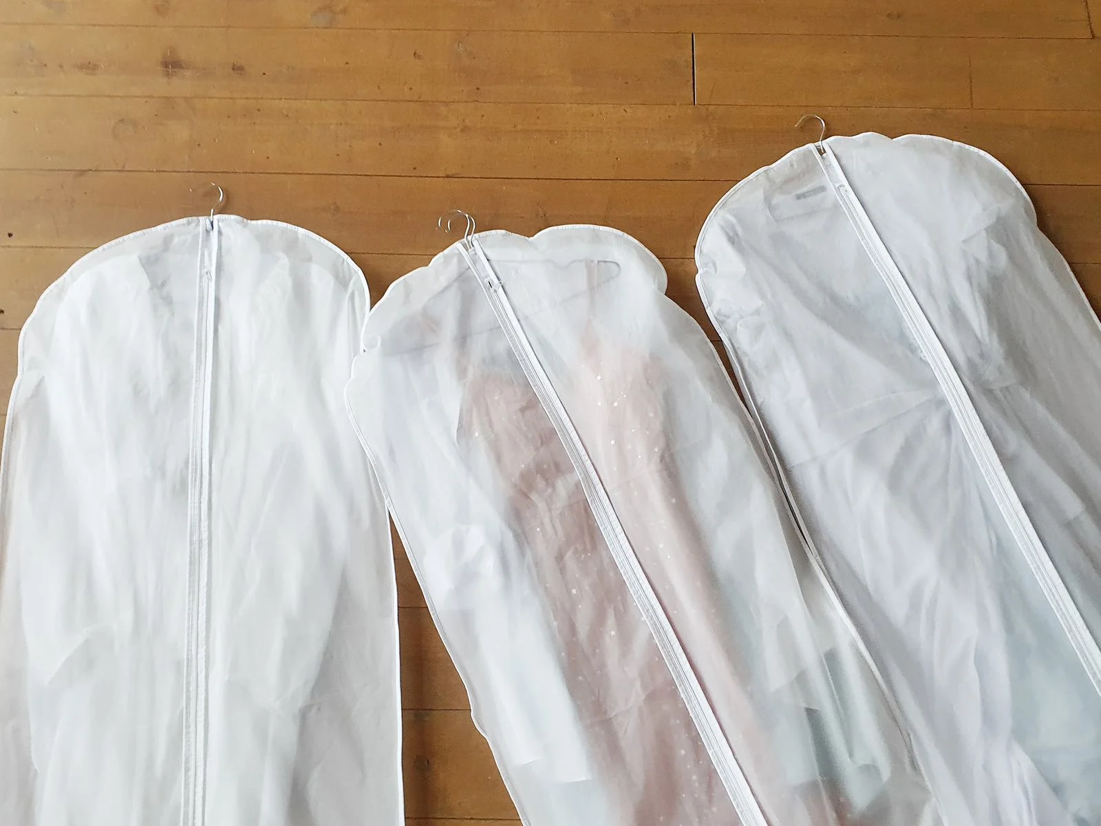 Layflat image of three of the best travel garment bags lying on a wooden table
