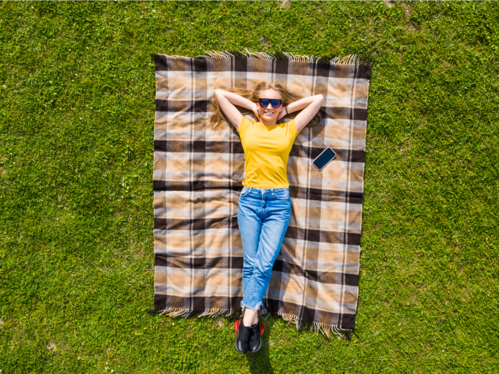 Woman lying on one of the best picnic blankets in a yellow shirt smiling and looking upward