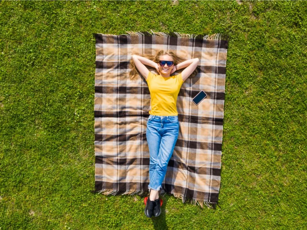 Woman lying on one of the best picnic blankets in a yellow shirt smiling and looking upward