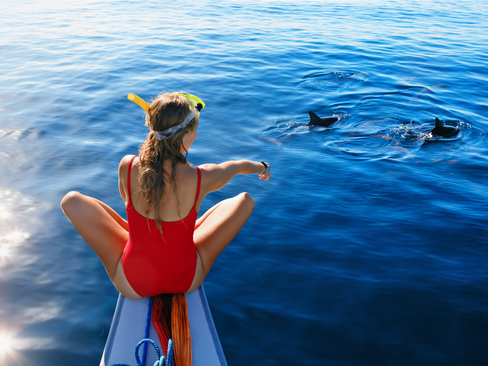 During the best time to visit Destin Florida, a woman in a red swimsuit sitting on a paddleboard looking at dolphins