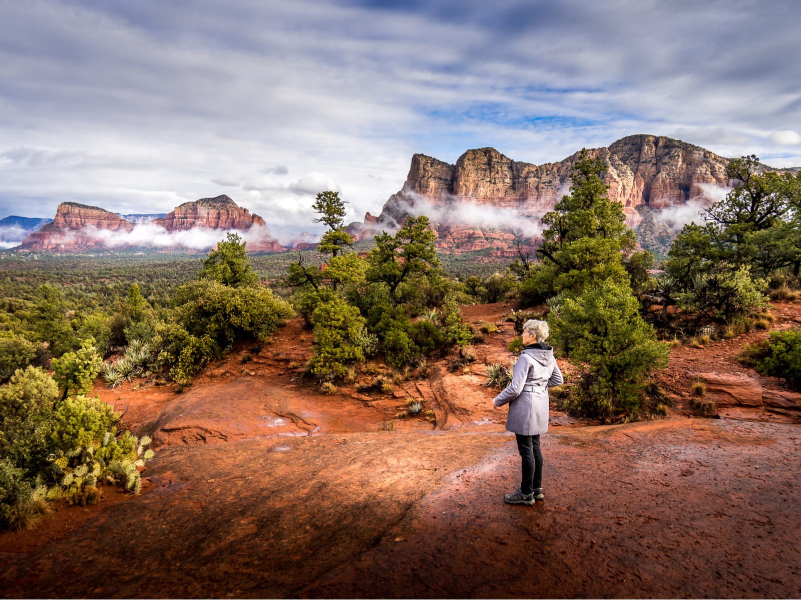 Woman standing in a Winter Coat with clouds over the hills during the cheapest time to visit Sedona