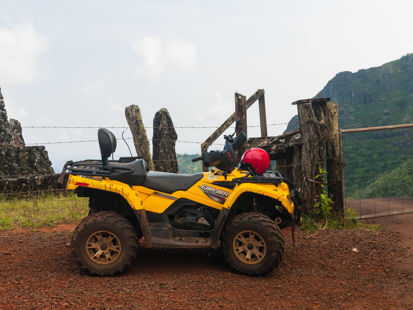 A muddy yellow ATV with a red helmet parked next to a barbed-wire fence, ATV riding is one of the best things to do in Kauai