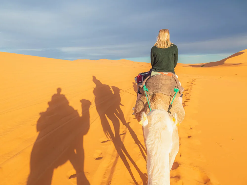 Cute blonde on a camel in the desert in a jacket during the best time to visit Morocco