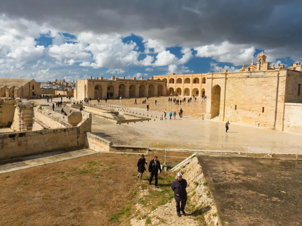 Heavy mass of clouds hovering above Fort Manoel in Malta, Game of Thrones filming locations you can visit, as a number of tourists stroll within the landmark