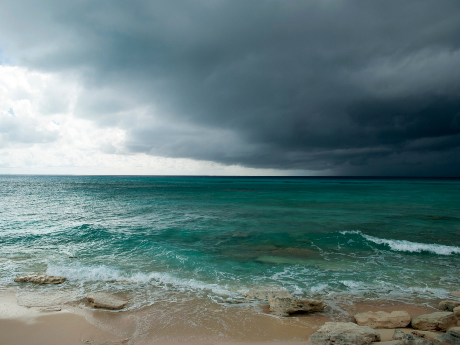 Stormy day over the ocean with rocks and a beach pictured during the worst time to visit Turks and Caicos