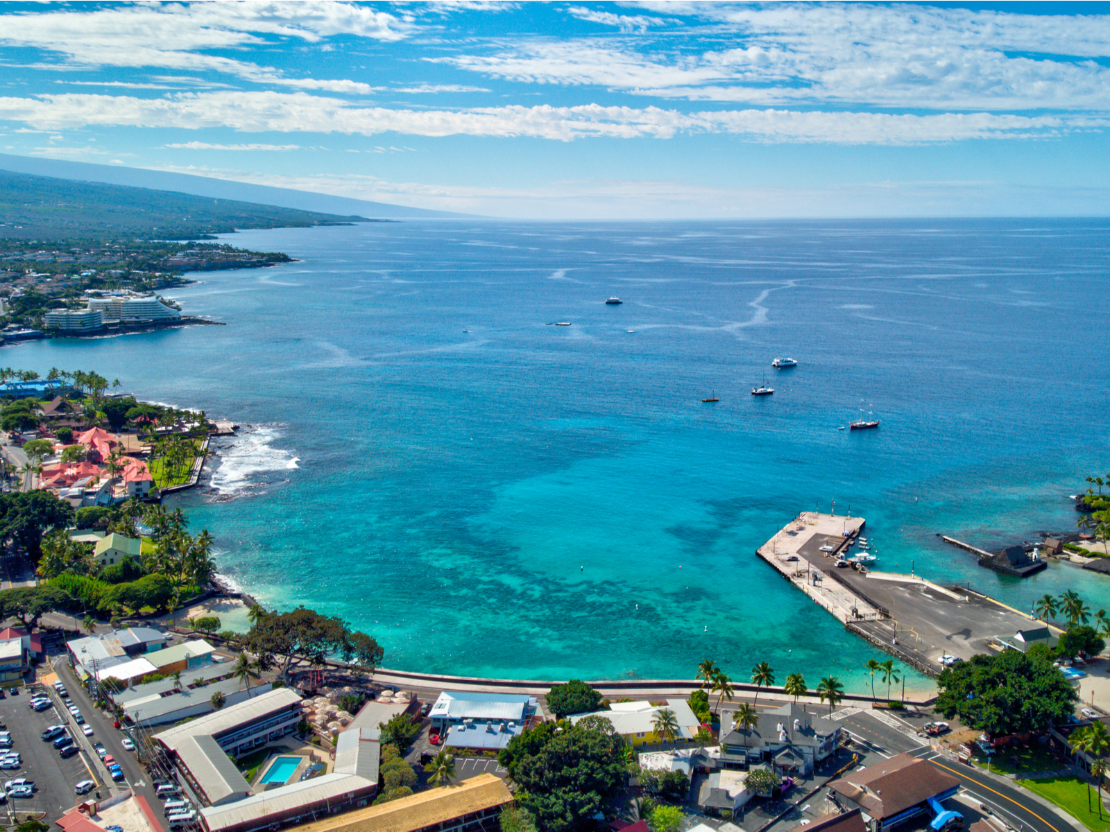 Aerial view on the peaceful Kailua-Kona Town structures as the best hotels in Kona, Hawaii, with few ships sailing on its calm emerald waters