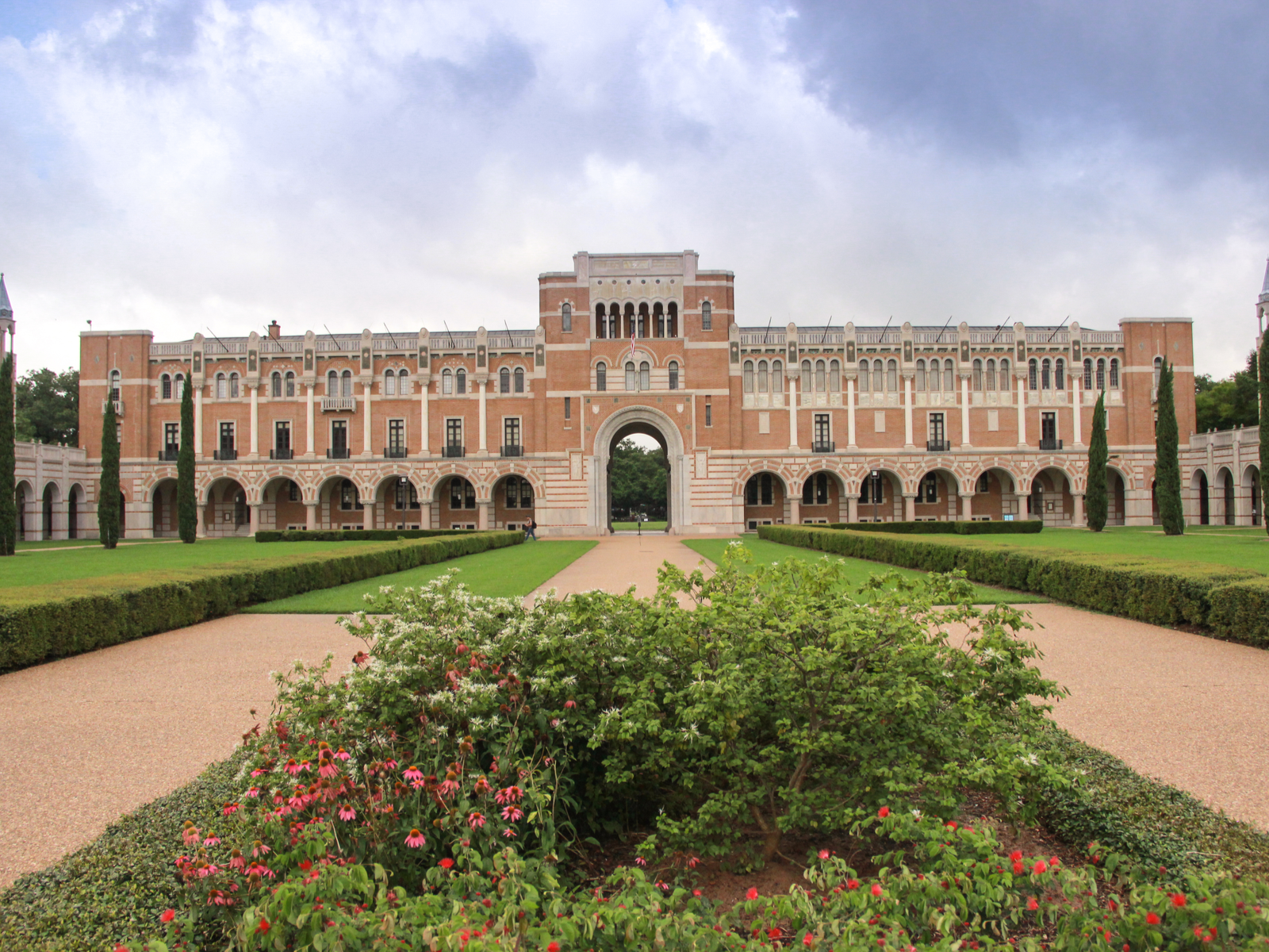 A wide building with an arch gate facing a beautiful landscape with trimmed bushes at Rice University in Texas, one of the most beautiful college campuses