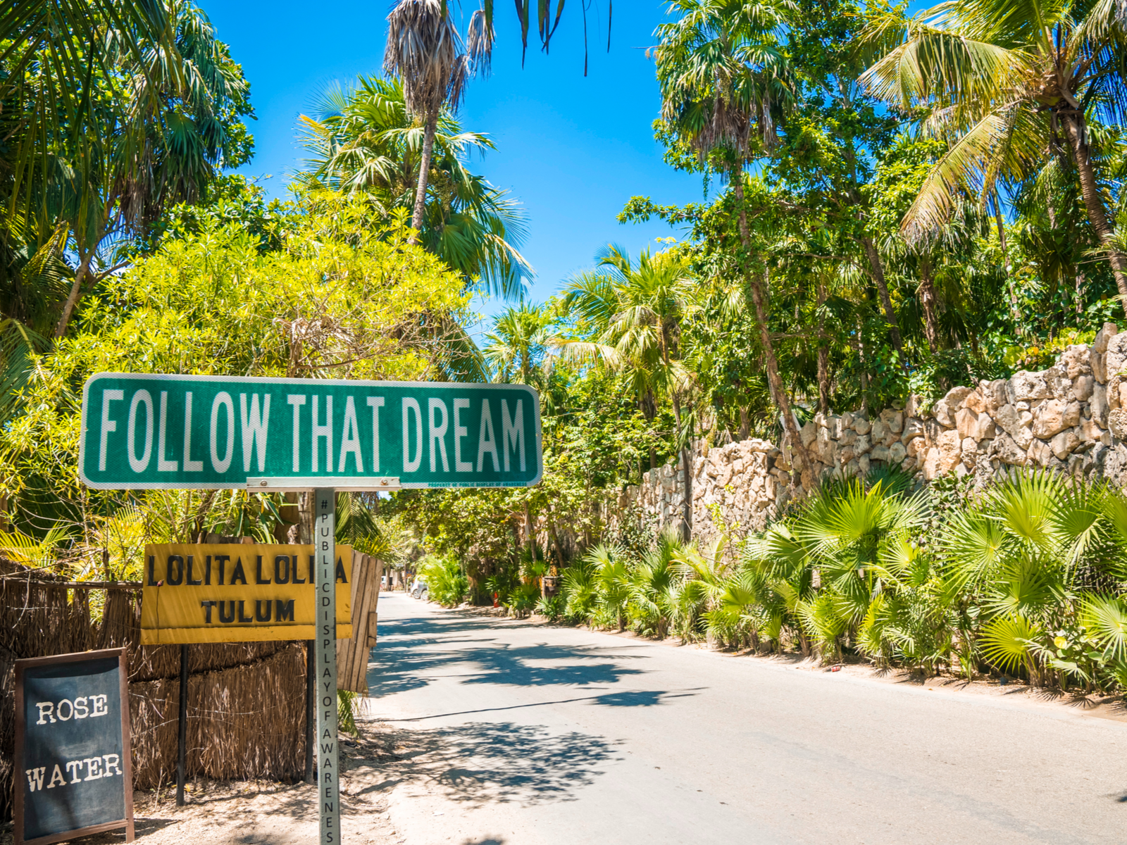 Sign that says follow that dream by a brick wall next to a road during the best time to go to Tulum Mexico