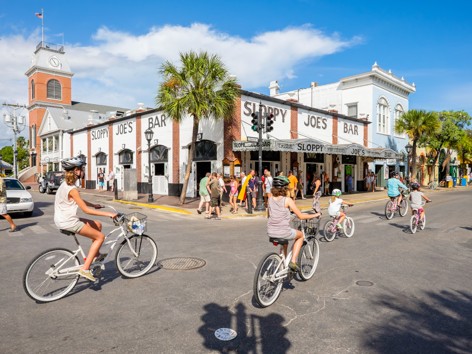 A family of five wearing helmets biking down the Duval Street and several people on the sidewalk beside Sloppy Joe's Bar, one of the best things to do in Key West