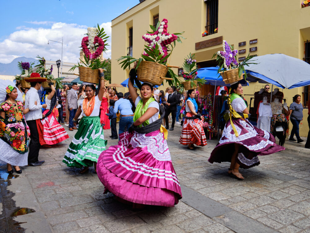 Woman in colorful dresses dancing in the streets for a piece titled Is Oaxaca Safe