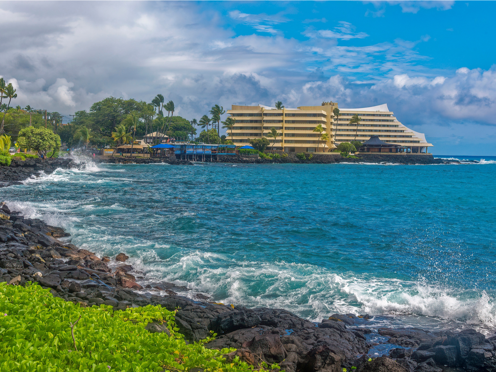 Wavy sea on the front of the Royal Kona Resort building, a piece on the best hotels in Kona, Hawaii, where palm trees are being blown by strong winds