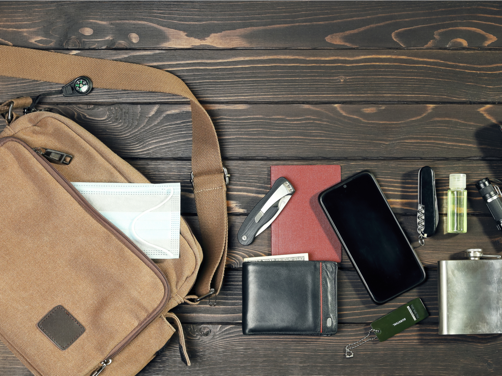 A bunch of stuff next to an urban EDC strap bag on a wooden table in a layflat image