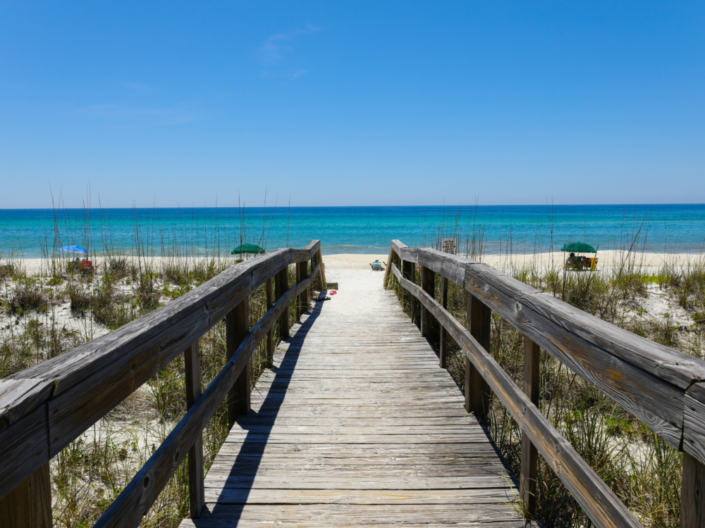 Beautiful view of a wooden bridge leading to a sandy beach on a sunny day during the best time to visit Destin Florida