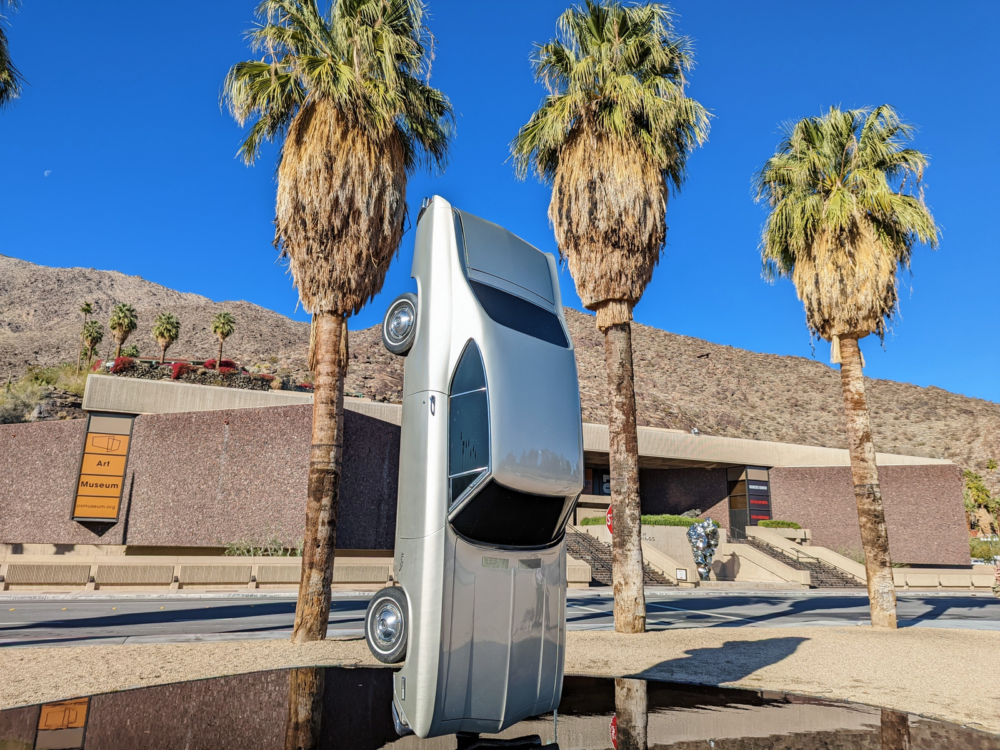 A monument of a car suspended in the air, title "History of Suspended Time: Monument for the Impossible" art installation by Gonzalo Lebrija, one of the best things to do in Palm Springs with the Palm Springs Art Museum in the backdrop