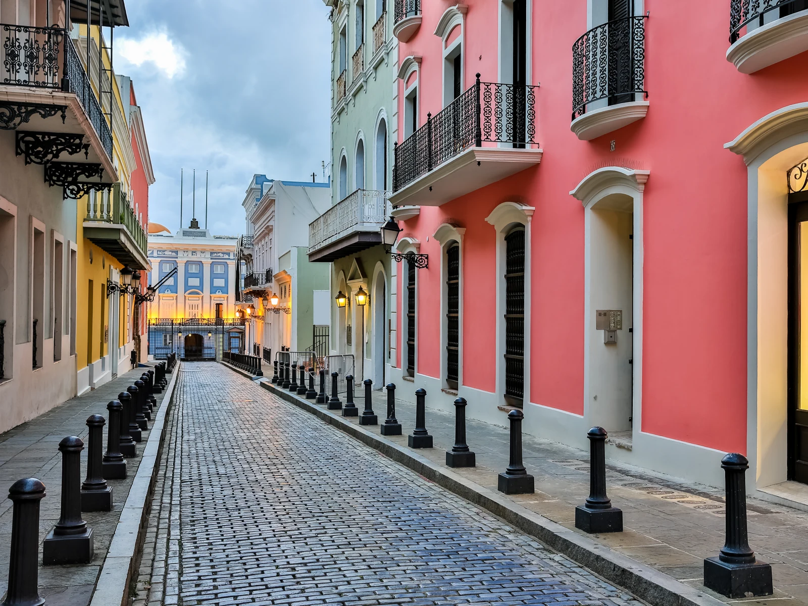 A brick street in Old San Juan, one of the best places to visit in Puerto Rico, with evenly spaced bollards beside vibrant structures