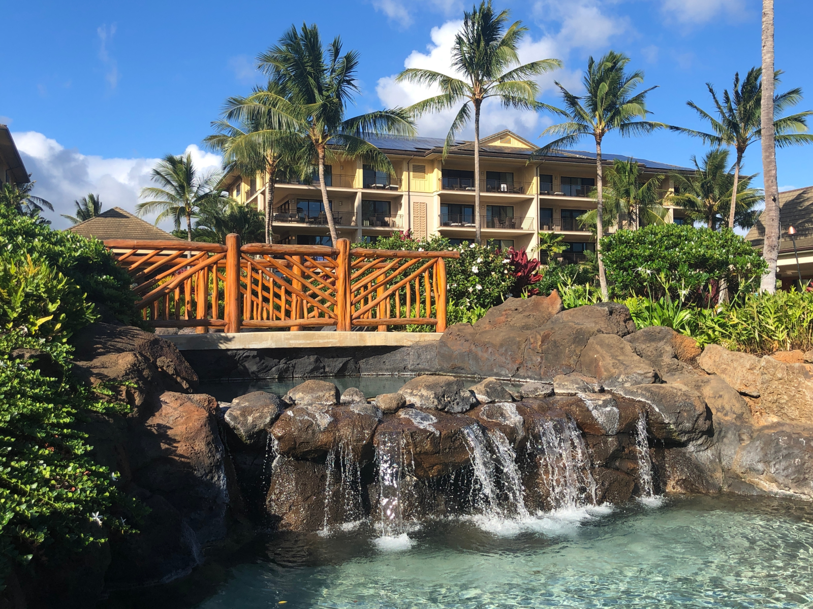 A small foot bridge with wooden railings and palm trees at the front of Koloa Landing Resort at Poipu, one of the best hotels in Kauai