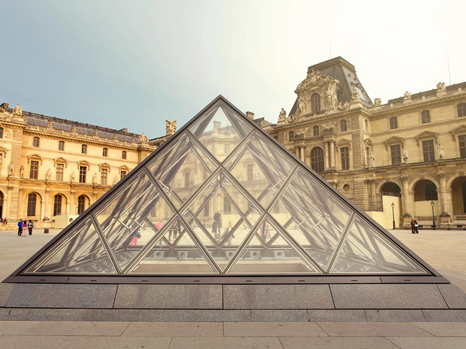 The Louvre pictured with its glass roof in the shape of a triangle on a cloudy day