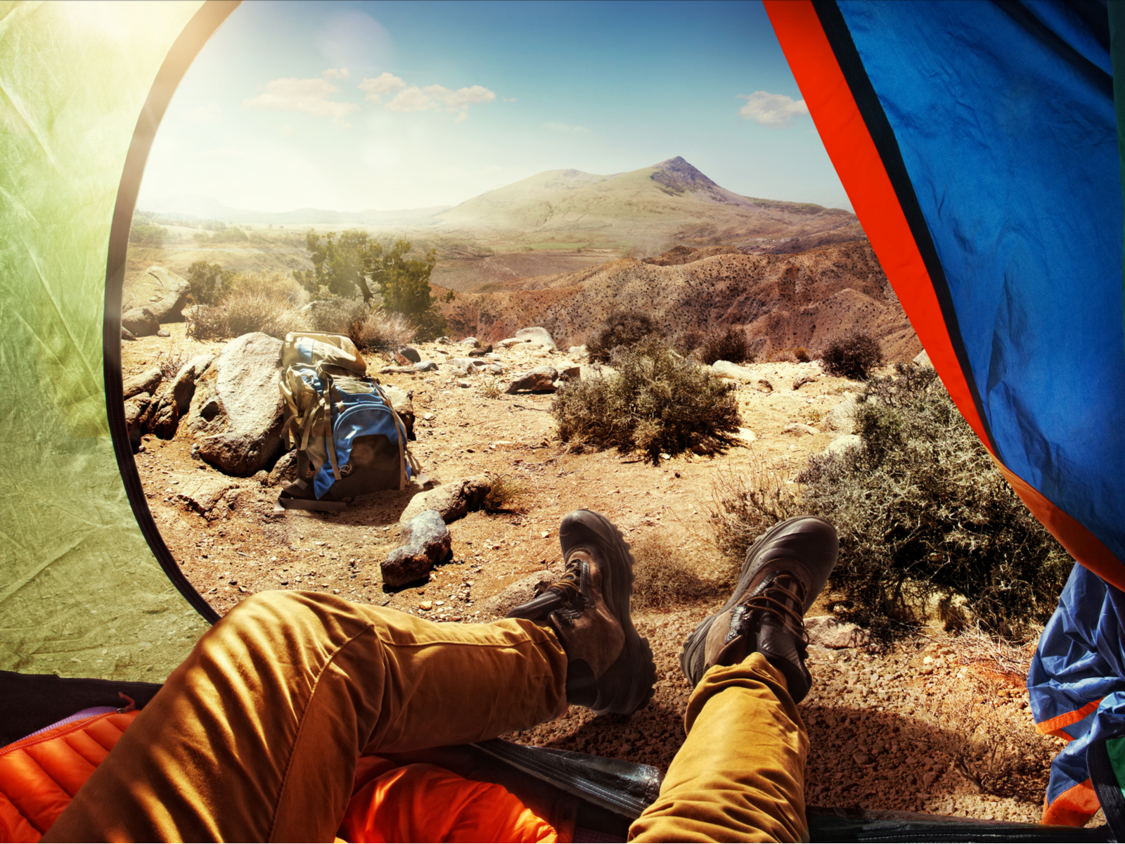 Guy with hiking boots and pants hanging out of one of the best one-man tents in the desert overlooking a mountain