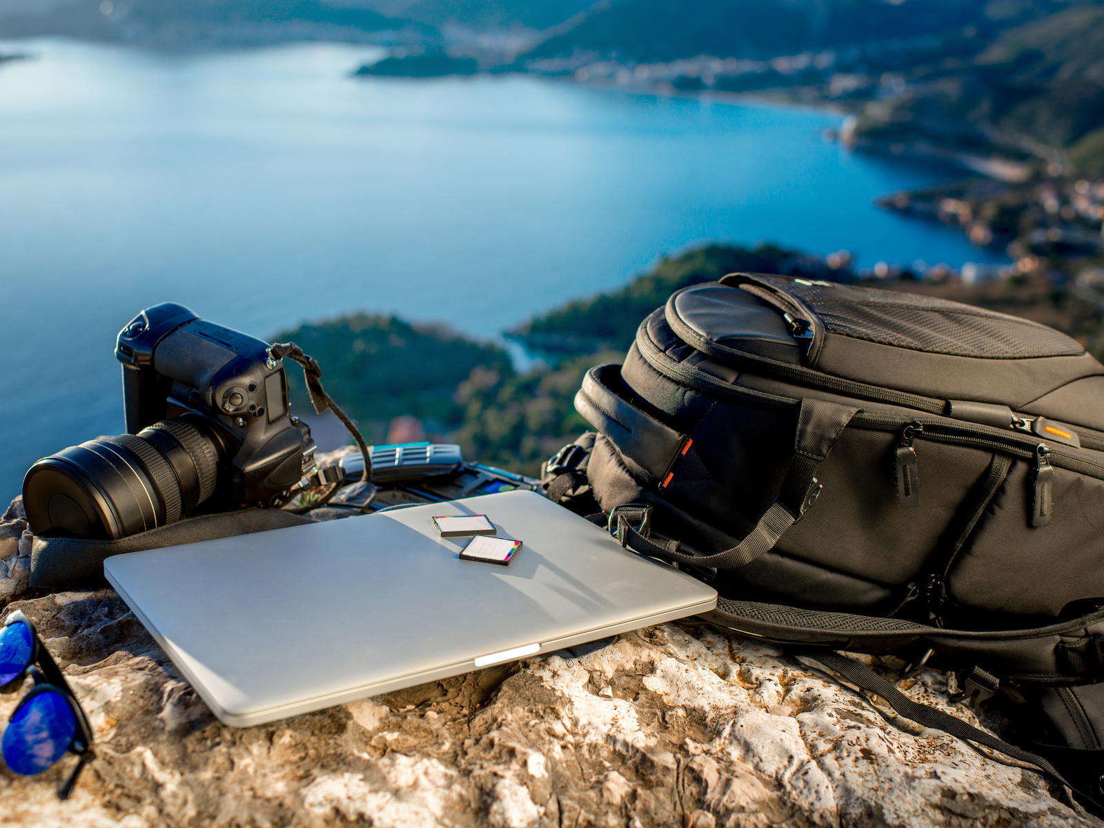 Photo of one of the best camera bags next to the camera and a laptop on a hill overlooking a lake