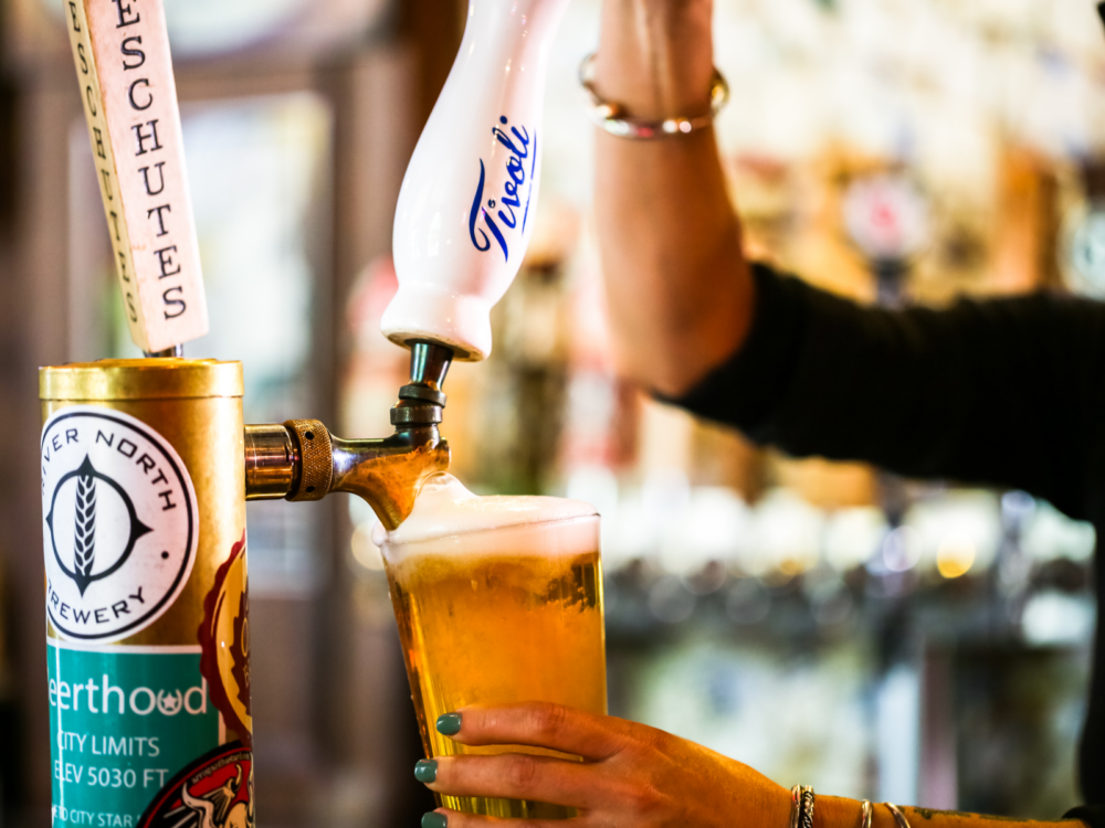 Arm in a black shirt pulling on a handle of a beer tap during the best time to visit Denver